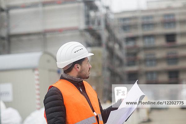 Man with plan wearing safety vest and hard hat at construction site