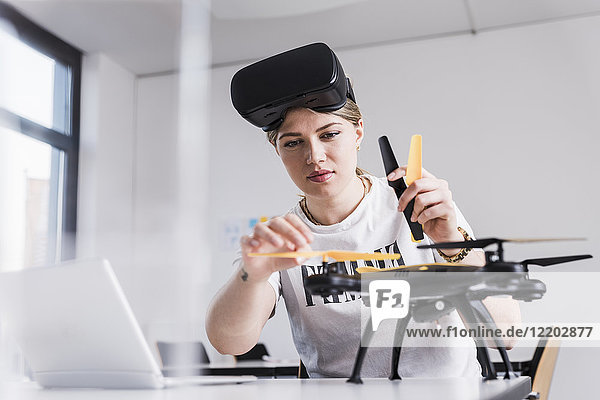 Young woman with laptop and VR glasses at desk examining drone