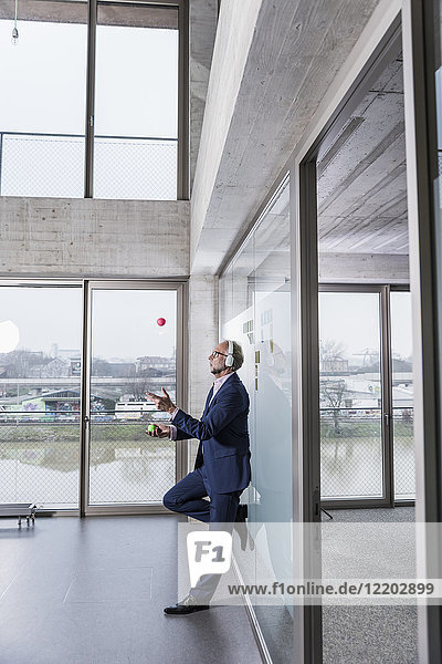 Mature businessman listening to music on headphones juggling with balls