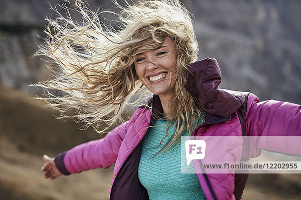 Glückliche junge Frau  die sich in den Bergen gegen den Wind lehnt.