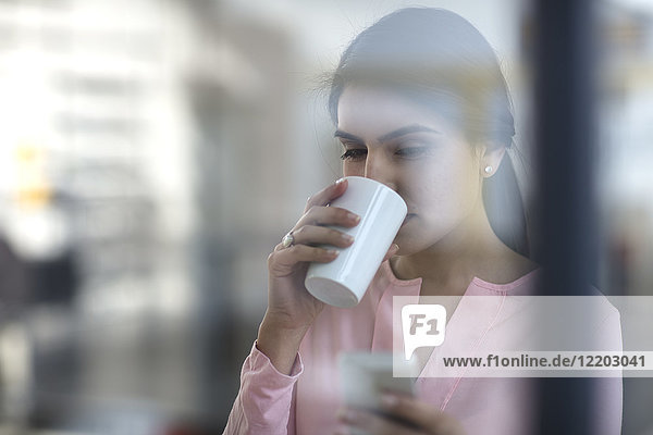 Porträt einer jungen Frau mit Handy und Kaffee im Büro