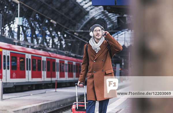 Junger Mann mit Gitarrenkoffer und Kopfhörer am Bahnsteig