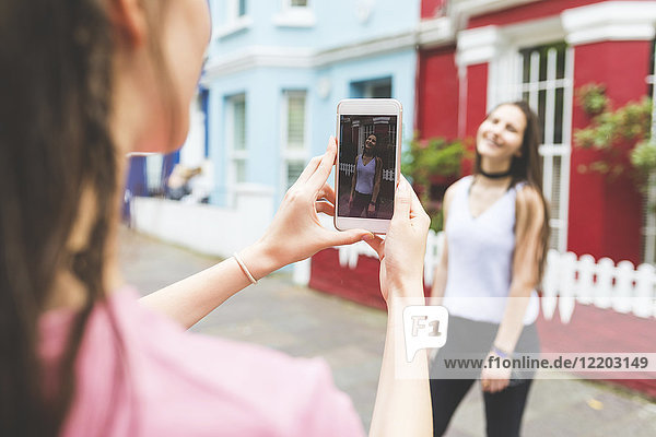 Young woman taking cell phone picture of teenage girl in the city