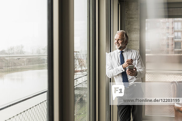 Smiling mature businessman standing at the window looking out
