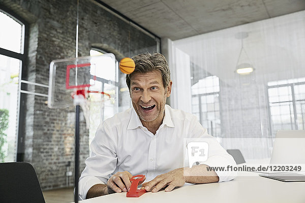 Glücklicher Geschäftsmann beim Minibasketballspiel im modernen Büro