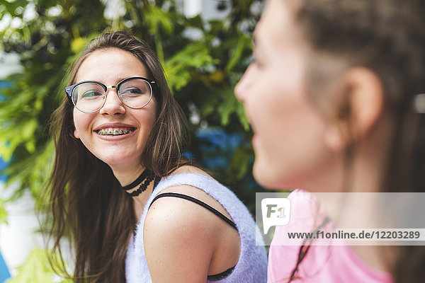 Happy teenage girl with braces and glasses looking at friend