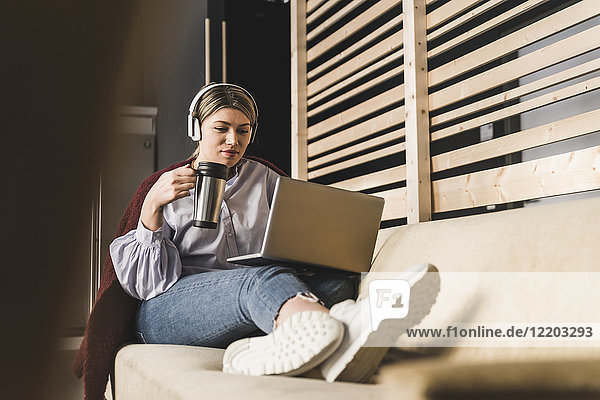 Junge Frau auf Couch mit Kaffee und Laptop