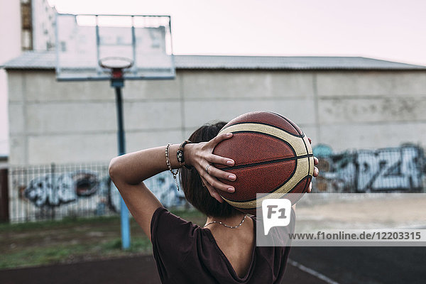 Rückansicht der jungen Frau mit Basketball auf dem Außenplatz
