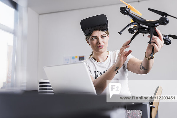 Junge Frau mit Laptop und VR-Brille am Schreibtisch mit Drohne
