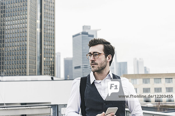 Deutschland  Frankfurt  junger Geschäftsmann mit Handy in der Stadt schaut sich um