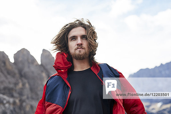 Porträt eines jungen Mannes mit windgepeitschten Haaren in den Bergen