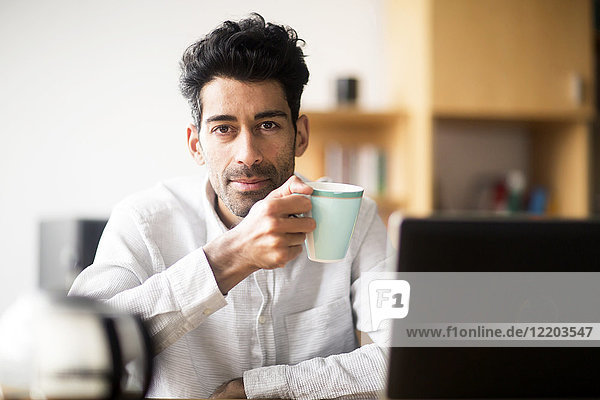 Portrait of relaxed businessman with mug at desk in the office