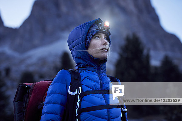 Junge Frau mit Stirnlampe bei Dämmerung in den Bergen