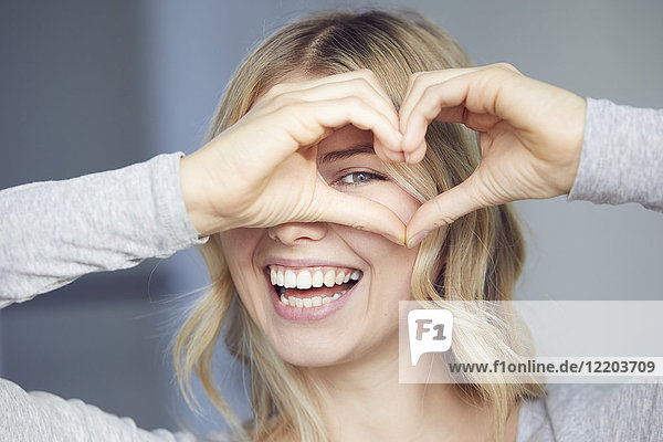 Porträt einer lachenden Frau  die mit ihren Fingern das Herz baut.