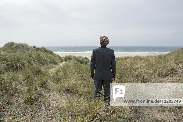 UK  Cornwall  Hayle  Geschäftsmann  der in Stranddünen steht und die Aussicht betrachtet