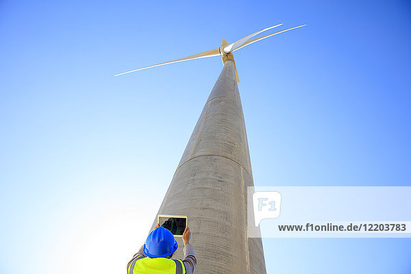 Low angle view of technician taking picture with a tablet of wind turbine