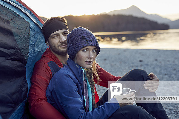 Young couple sitting at tent at lakeshore