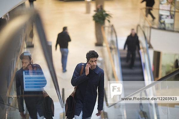 Mann am Telefon steht auf einer Rolltreppe in einem Einkaufszentrum