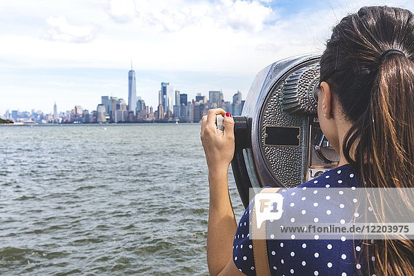 USA  New York  Frau mit Blick auf die Skyline von Manhattan mit Münzfernrohr