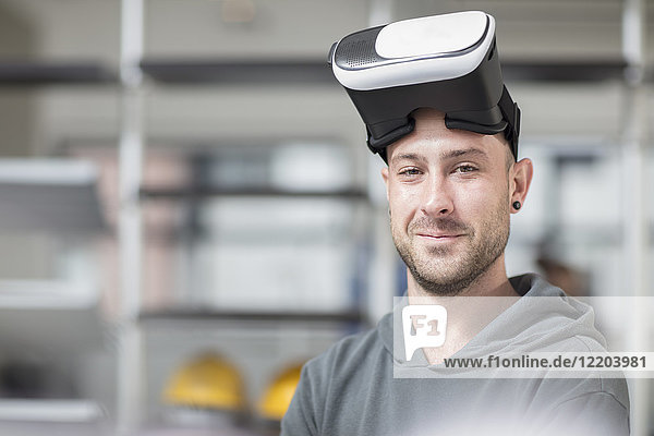 Porträt eines lächelnden jungen Mannes mit VR-Brille im Büro