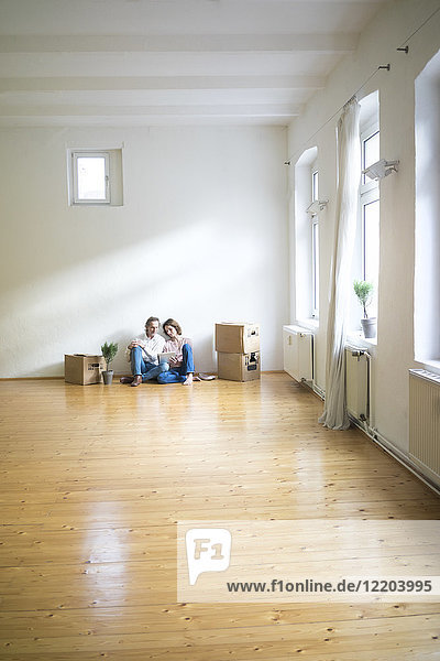 Das reife Paar sitzt auf dem Boden in einem leeren Raum neben den Kartons mit Tabletten.