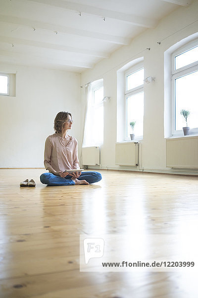 Reife Frau auf dem Boden sitzend in leerem Raum mit Tablette