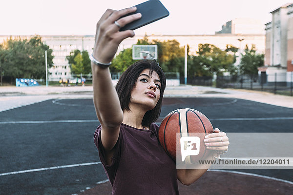 Junge Frau mit Basketball  die einen Selfie auf dem Freigelände nimmt.