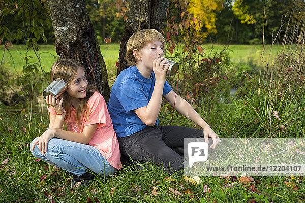Boy and girl on a meadow having fun with tin can phone