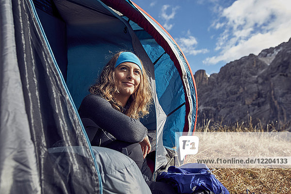 Lächelnde junge Frau im Zelt in den Bergen sitzend