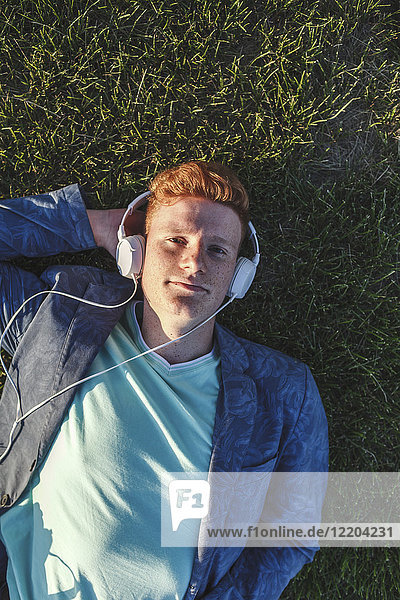 Porträt eines rothaarigen jungen Mannes mit Kopfhörer auf Gras liegend