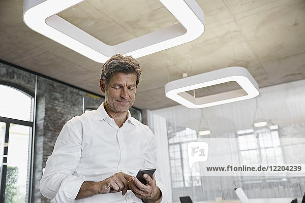 Ausgereifter Geschäftsmann mit Smartphone im modernen Büro