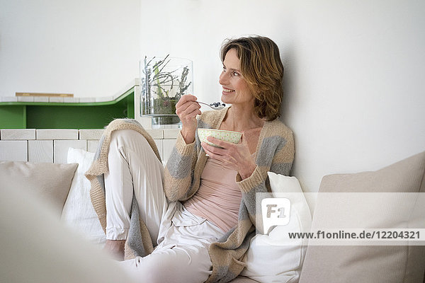 Relaxed smiling mature woman sitting on bench eating healthy food