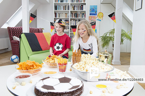 Brother and sister watching football world cup with sweets and snacks