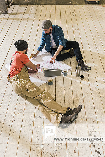 Zwei Männer mit Laptop beim Betrachten des Bauplans auf dem Boden