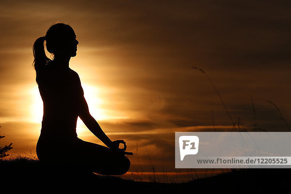 Silhouette of a woman in lotus position  practising yoga against the light of the evening sun  French Alps  France  Europe