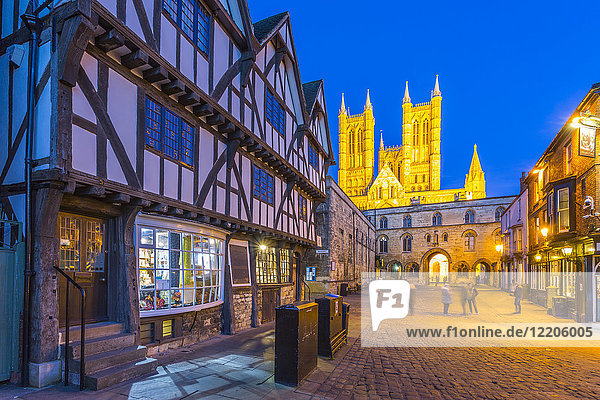 View of illuminated Lincoln Cathedral viewed from Exchequer Gate with timbered architecture of Visitors Centre at dusk  Lincoln  Lincolnshire  England  United Kingdom  Europe