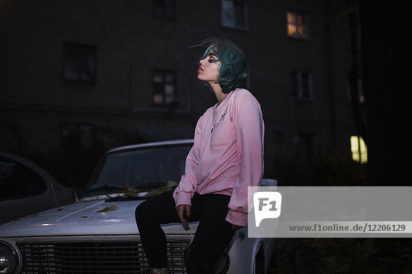 Kaukasische Frau sitzt nachts auf der Motorhaube eines Autos