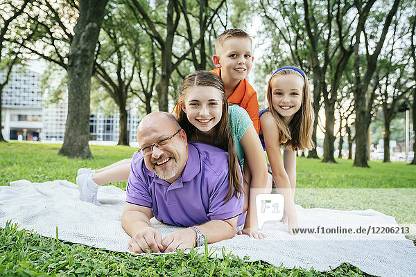 Portrait of Caucasian boy and girls laying on back of father in park