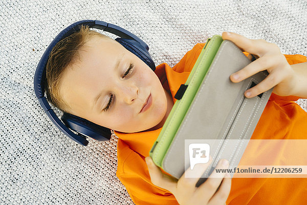 Smiling Caucasian boy laying on blanket listening to digital tablet