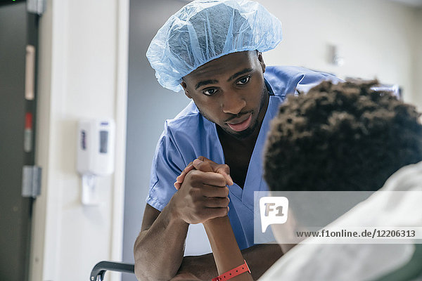 Schwarzer Arzt hält Hand eines Jungen im Krankenhausbett