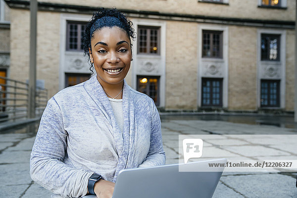 Porträt einer lächelnden schwarzen Frau  die im Freien einen Laptop benutzt