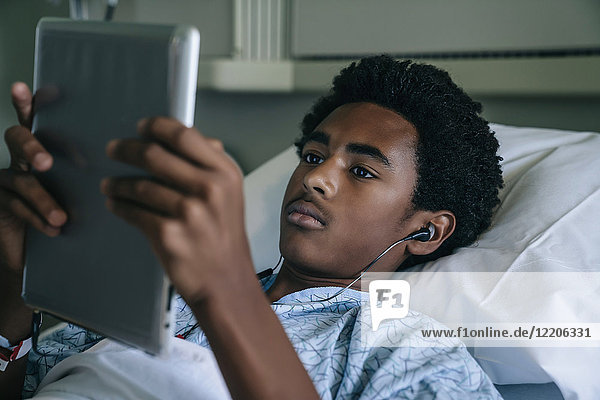 Black boy laying in hospital bed listening to digital tablet