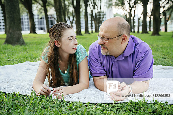 Serious Caucasian father and daughter talking on blanket in park