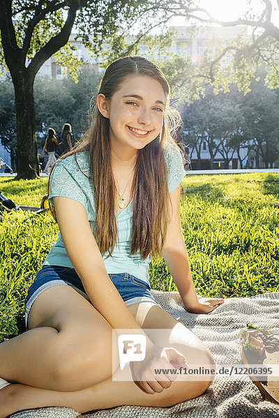 Porträt eines lächelnden kaukasischen Mädchens  das auf einer Decke im Park sitzt