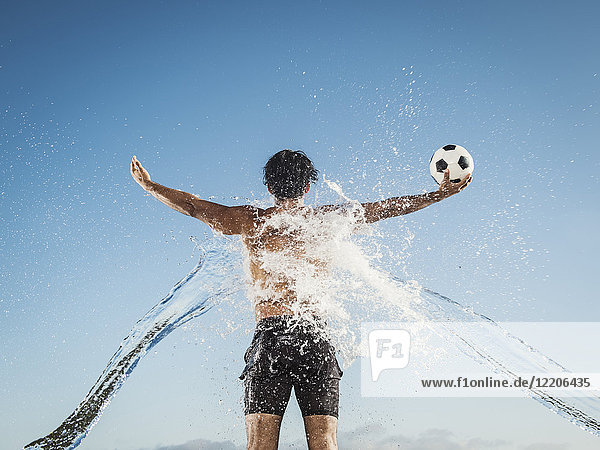 Wasser spritzt auf den Rücken eines hispanischen Mannes  der einen Fußball hält