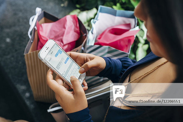 Hispanische Frau mit Einkaufstüten  die eine SMS auf ihrem Handy schreibt