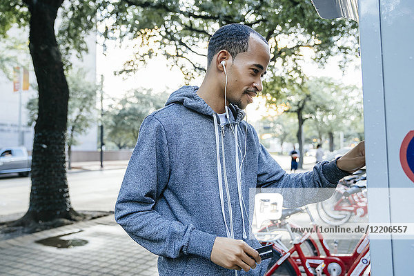 Schwarzer Mann mit Ohrstöpseln,  der mit Kreditkarte für einen Fahrradverleih bezahlt