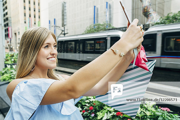 Kaukasische Frau mit Einkaufstasche posiert für Handy-Selfie