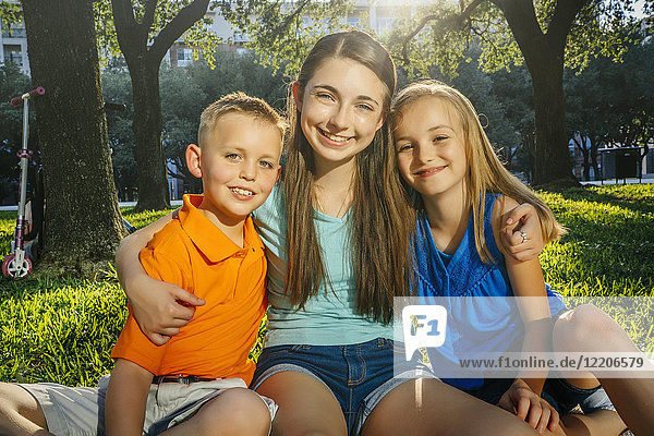 Portrait of smiling Caucasian brother and sisters hugging in park