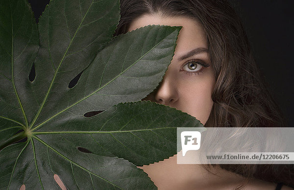 Kaukasische Frau versteckt sich hinter grünem Blatt